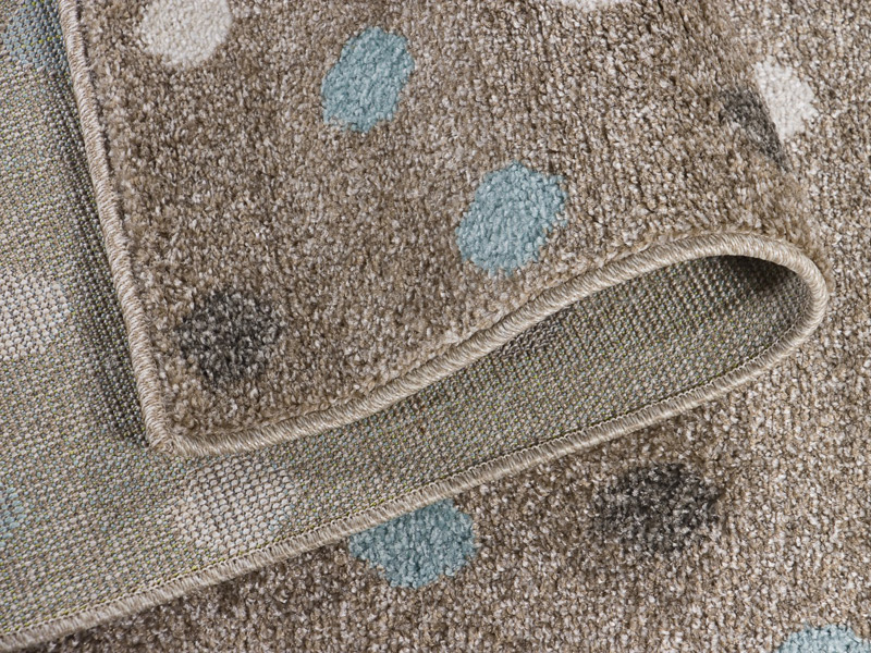 Zbliżenie zawiniętego fragmentu sztucznego dywanu polipropylenowego w kolorach beżu w białe i błękitne kropki. Widoczny efekt czyszczenia ekstrakcyjnego.