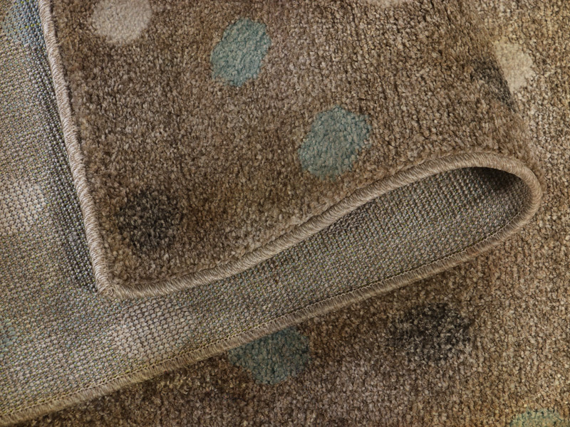 Zbliżenie zawiniętego fragmentu sztucznego dywanu polipropylenowego w kolorach beżu w białe i błękitne kropki. Widoczne silne zabrudzenie dywanu.